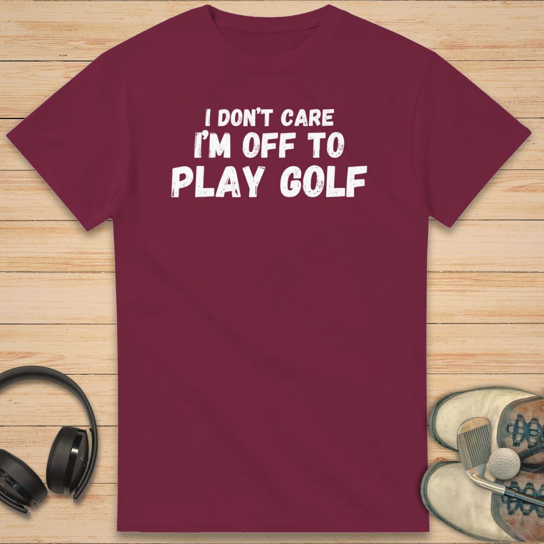 Don't Care T-Shirt in Maroon on a light wooden floor lying next to headphones and golf shoes.