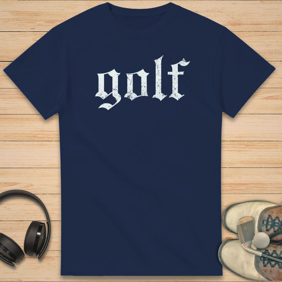 Gothic Golf T-Shirt in Navy on a light wooden floor lying next to headphones and golf shoes.