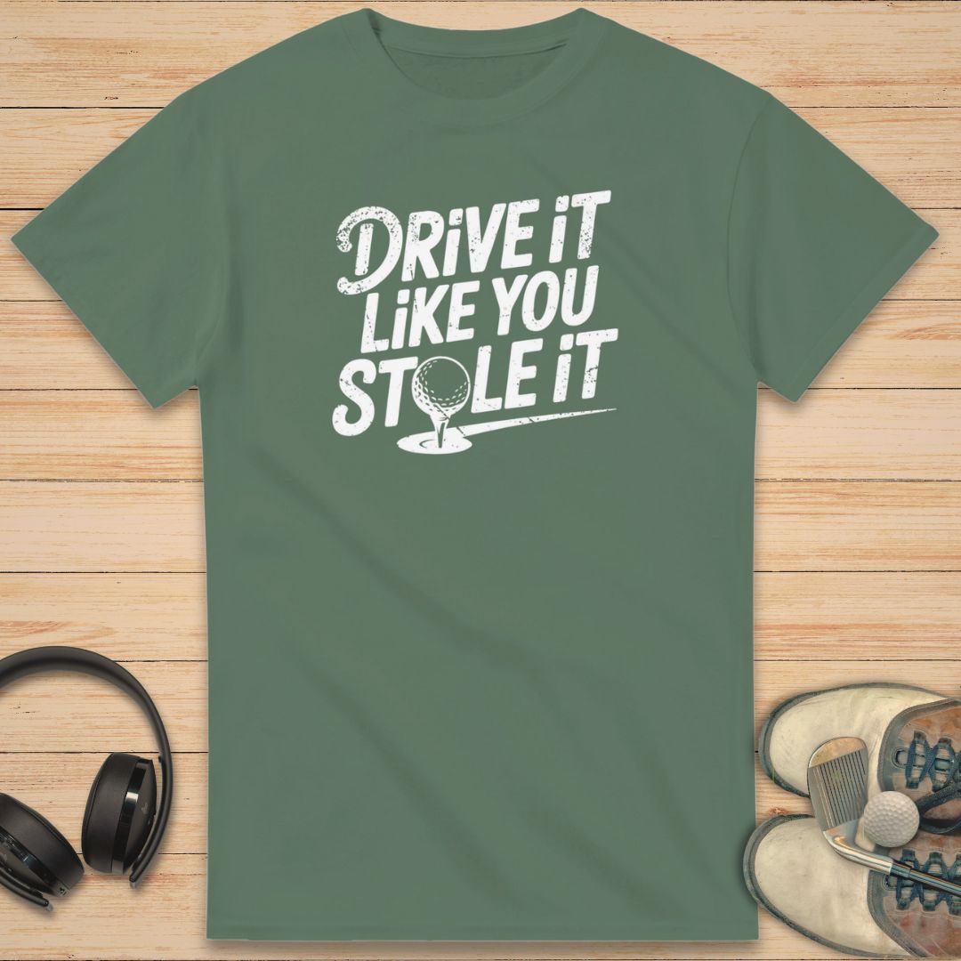 Stole It T-Shirt in Military Green on a light wooden floor lying next to headphones and golf shoes.