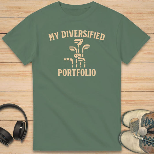 Portfolio T-Shirt in Military Green on a light wooden floor lying next to headphones and golf shoes.