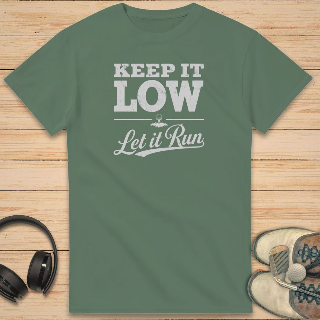 Keep It Low T-Shirt in Military Green on a light wooden floor lying next to headphones and golf shoes.