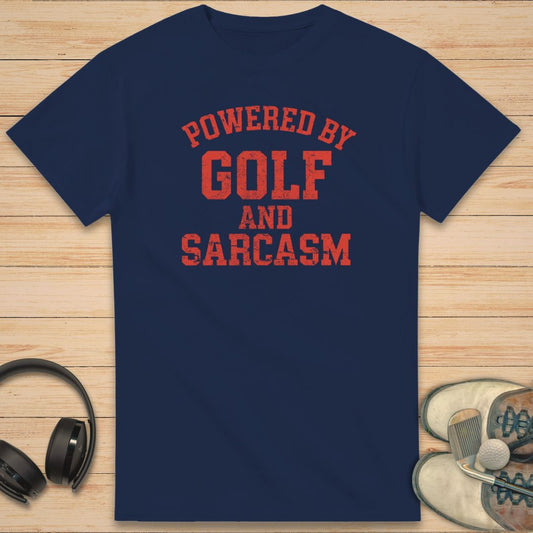 Powered By T-Shirt in Navy on a light wooden floor lying next to headphones and golf shoes.