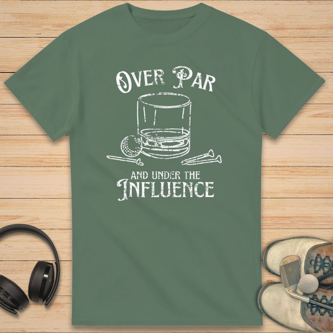 Over Par T-Shirt in Military Green on a light wooden floor lying next to headphones and golf shoes.
