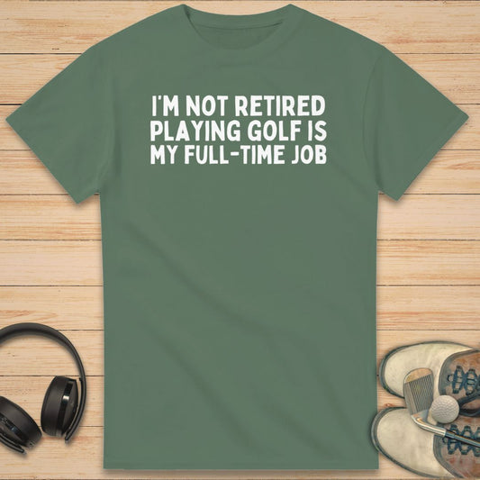 Full-Time Job T-Shirt in Military Green on a light wooden floor lying next to headphones and golf shoes.