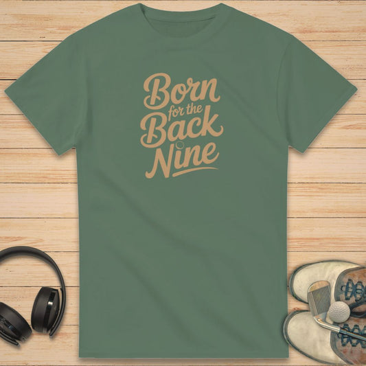 Back Nine T-Shirt in Military Green on a light wooden floor lying next to headphones and golf shoes.