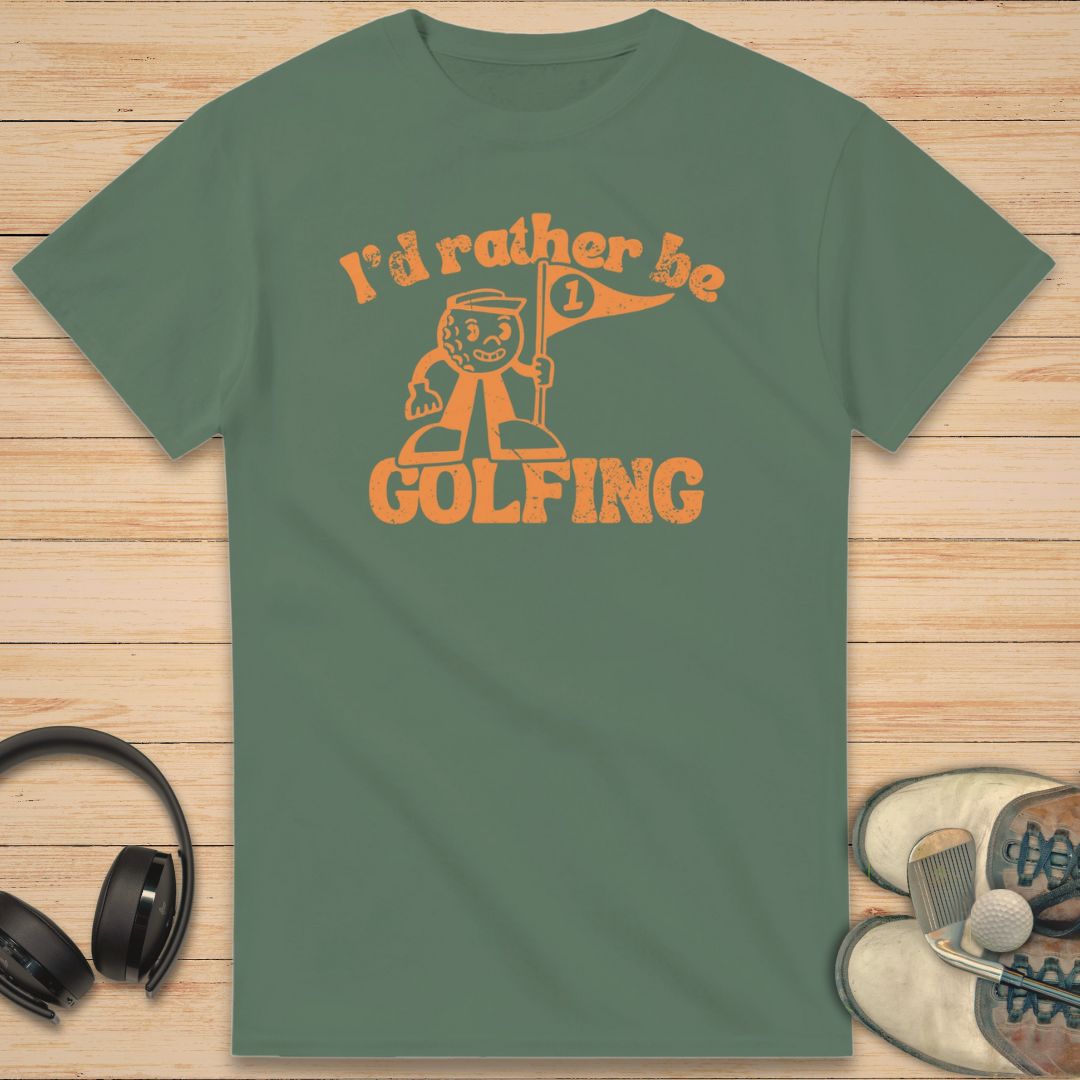 Be Golfing Mascot T-Shirt in Military Green on a light wooden floor lying next to headphones and golf shoes.