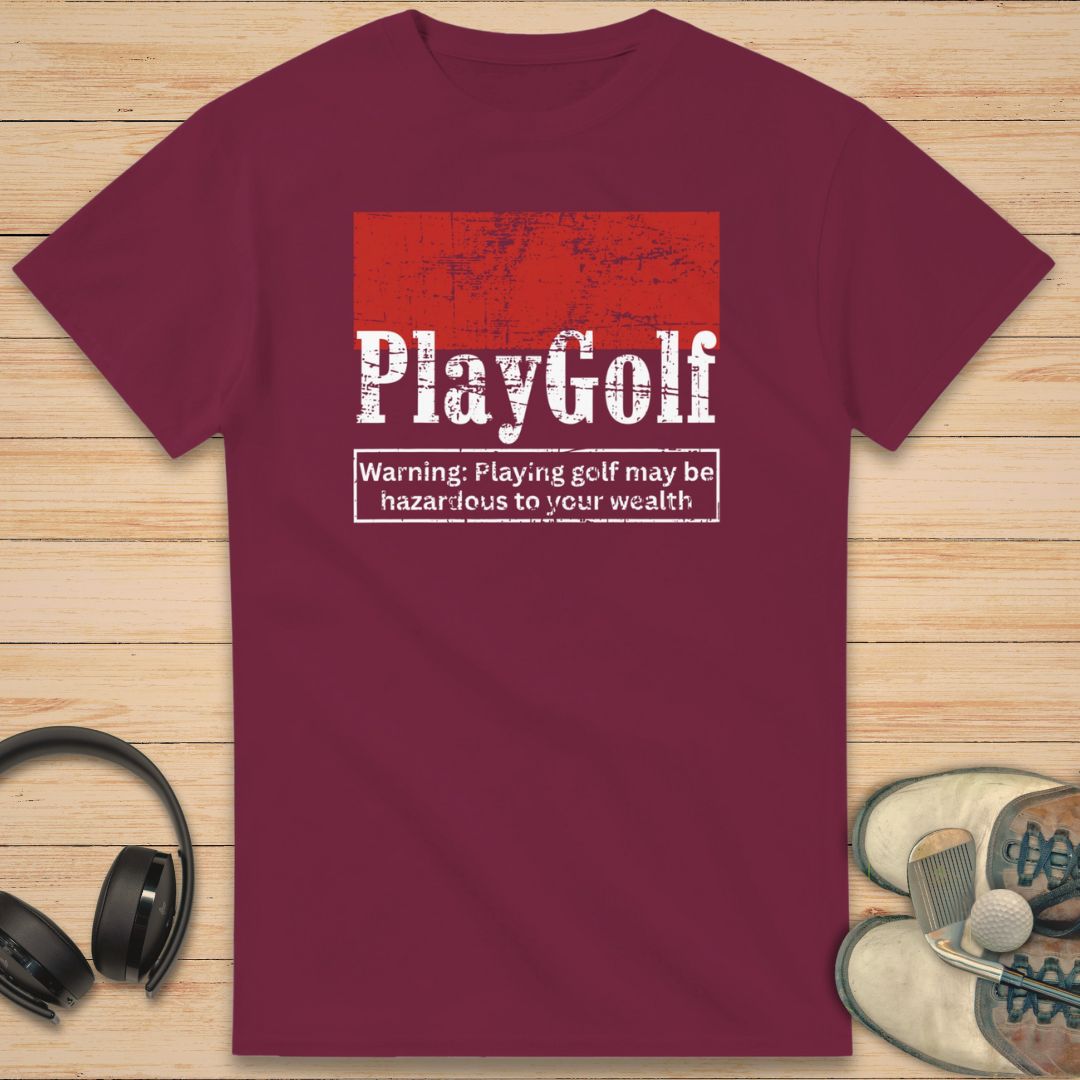 Play Golf T-Shirt in Maroon on a light wooden floor lying next to headphones and golf shoes.