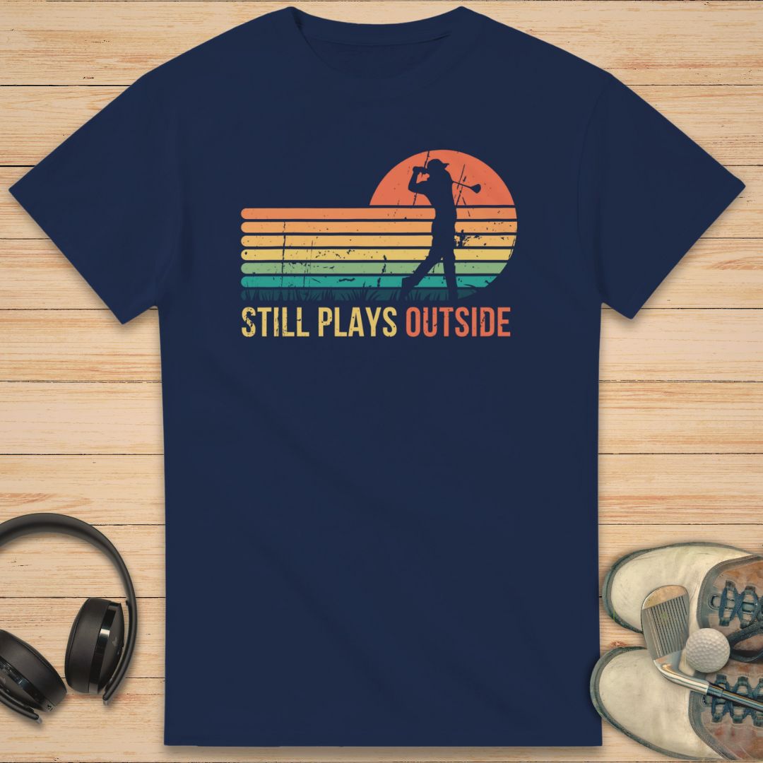 Plays Outside T-Shirt in Navy on a light wooden floor lying next to headphones and golf shoes.