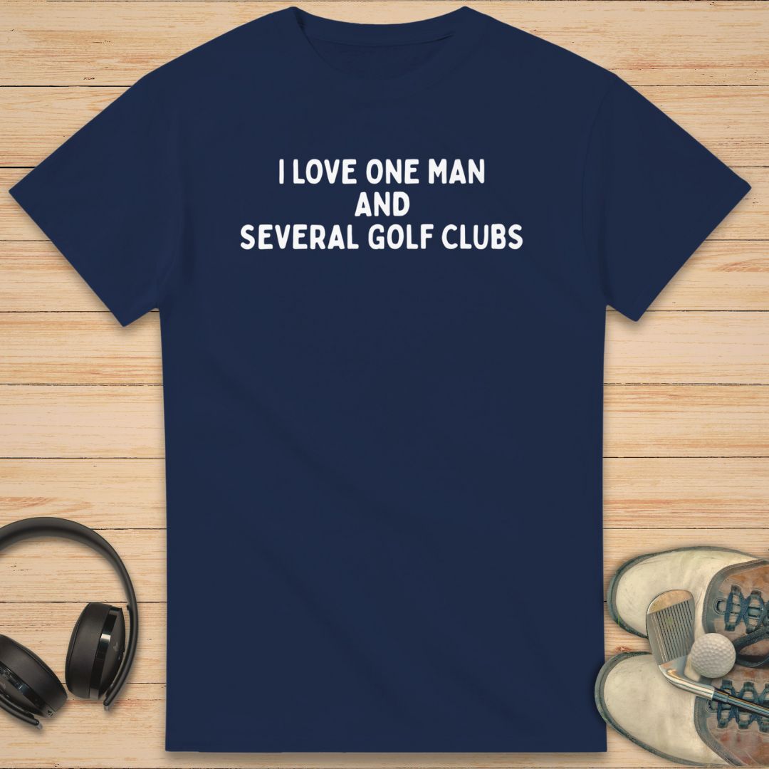 One Man T-Shirt in Navy on a light wooden floor lying next to headphones and golf shoes.