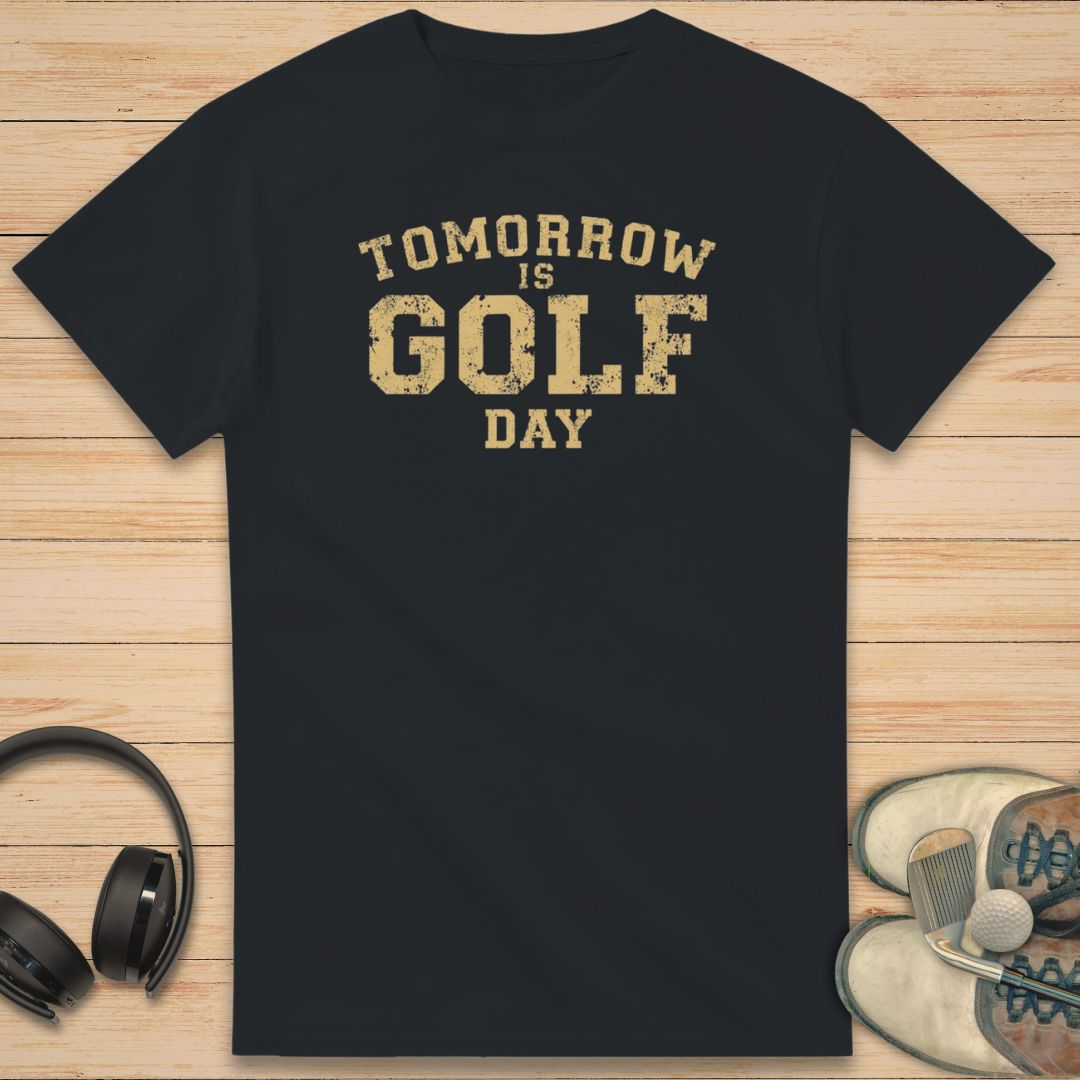 Golf Day T-Shirt in Black on a light wooden floor lying next to headphones and golf shoes.