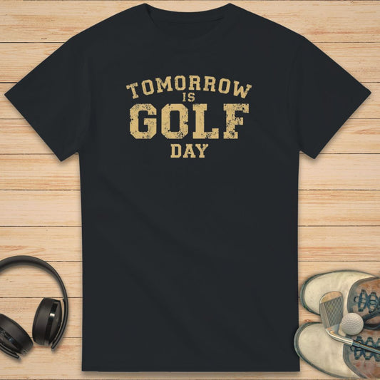 Golf Day T-Shirt in Black on a light wooden floor lying next to headphones and golf shoes.
