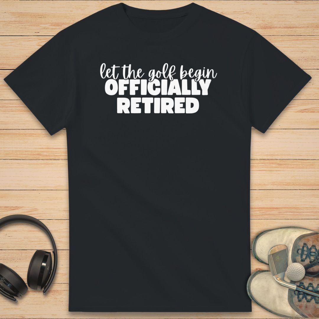 Golf Begin T-Shirt in Black on a light wooden floor lying next to headphones and golf shoes.