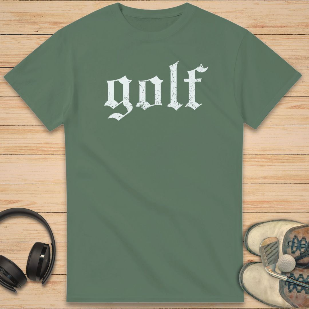 Gothic Golf T-Shirt in Military Green on a light wooden floor lying next to headphones and golf shoes.