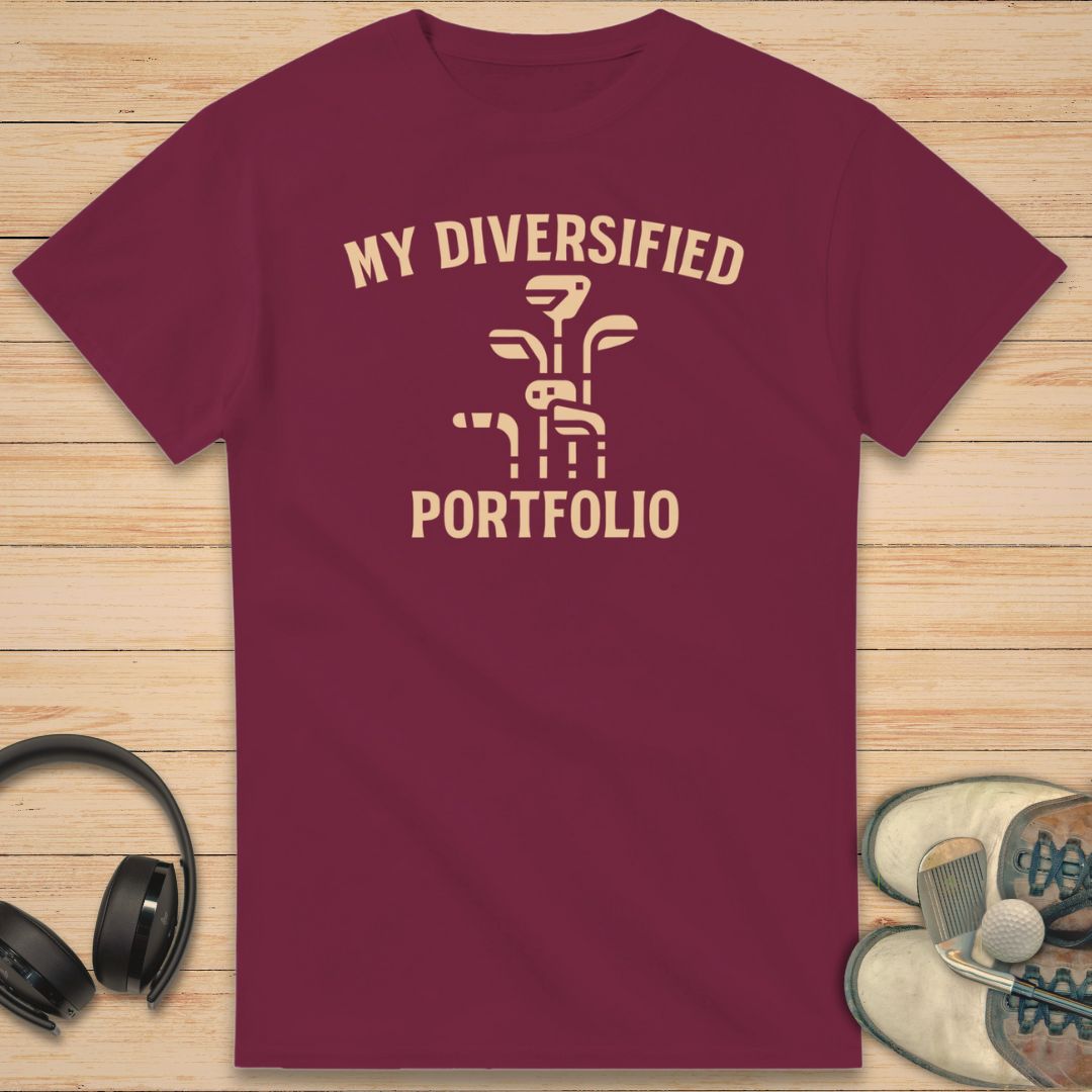Portfolio T-Shirt in Maroon on a light wooden floor lying next to headphones and golf shoes.