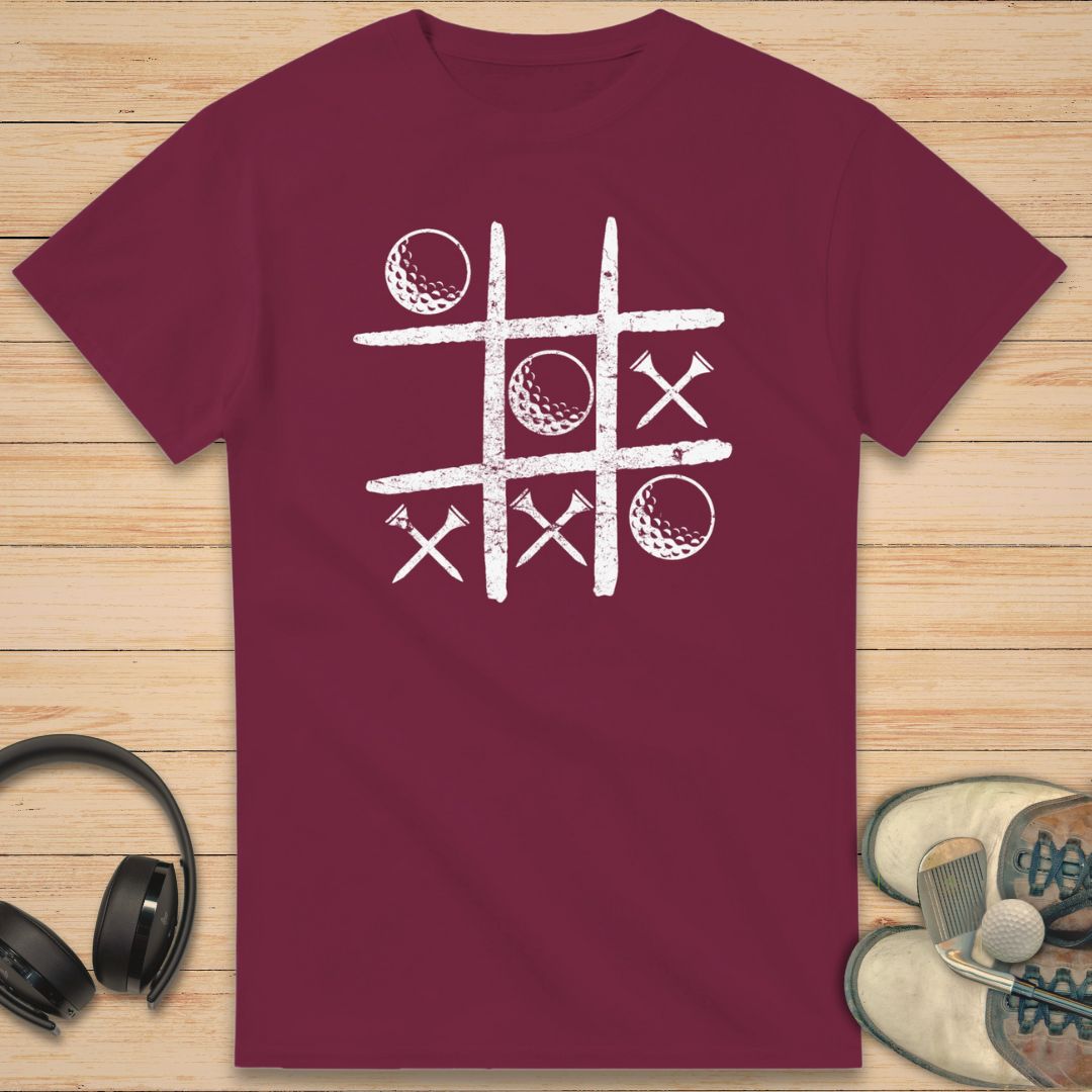 Balls And Tees T-Shirt in Maroon on a light wooden floor lying next to headphones and golf shoes.