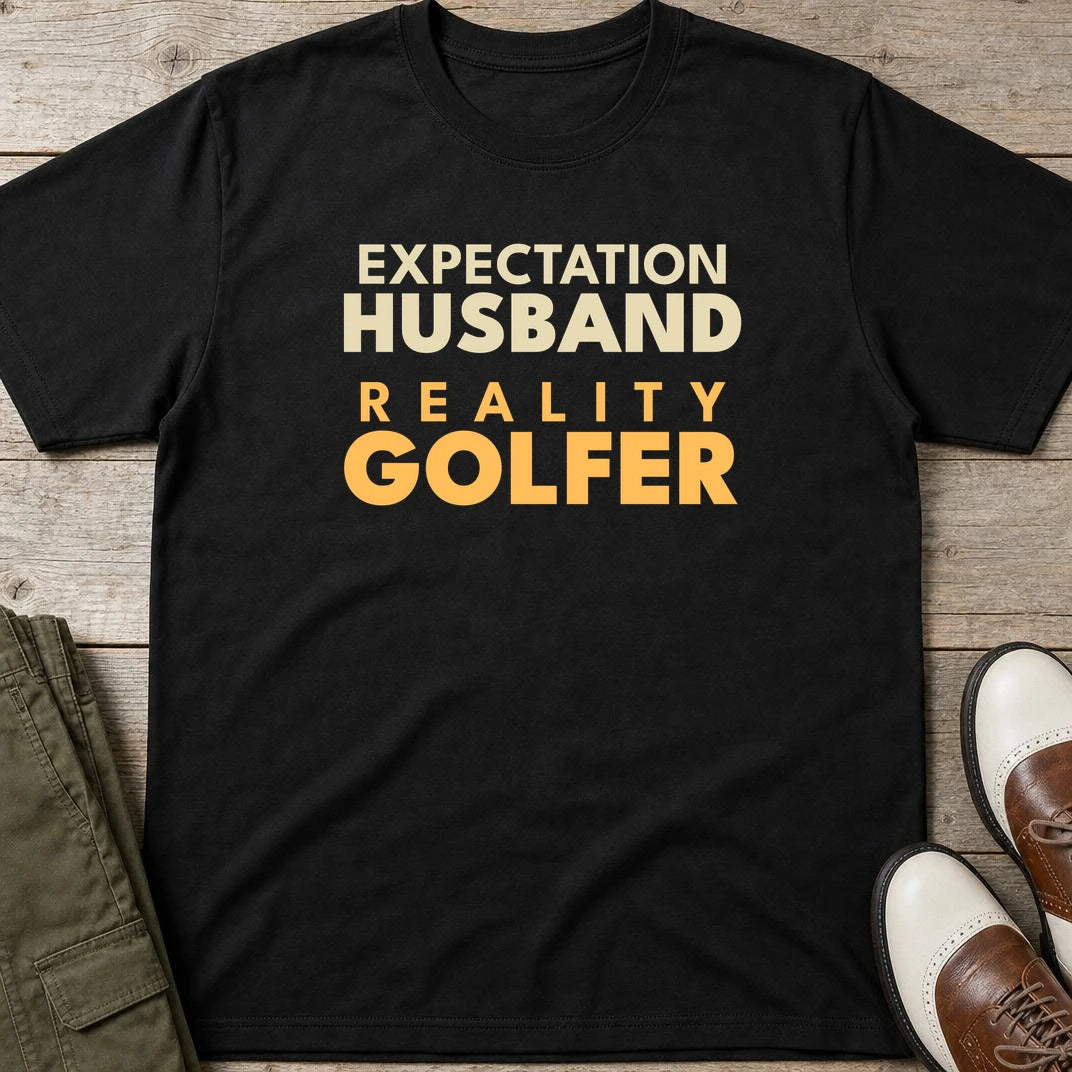 Reality Golfer T-Shirt in Black lying on a plain floor. T-shirt is a unisex cut and 100 per cent cotton.