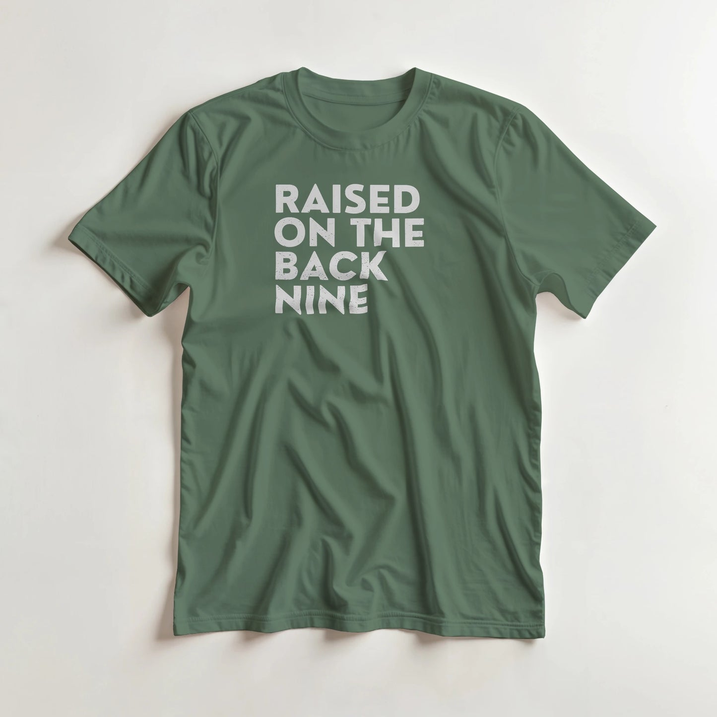 Raised On T-Shirt in Military Green lying on a plain floor. T-shirt is a unisex cut and 100 per cent cotton.