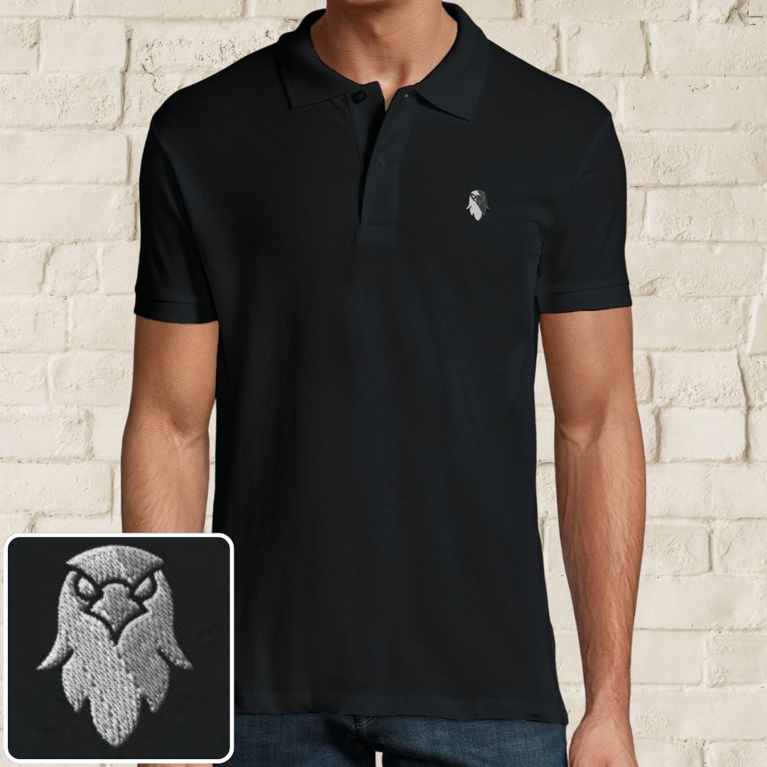 Eagle Polo in Black on a light wooden floor lying next to headphones and golf shoes.