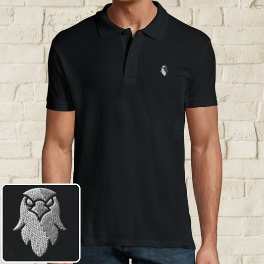 Eagle Polo in Black on a light wooden floor lying next to headphones and golf shoes.