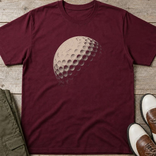 Golf Ball Grit T-Shirt in Maroon lying on a plain floor. T-shirt is a unisex cut and 100 per cent cotton.