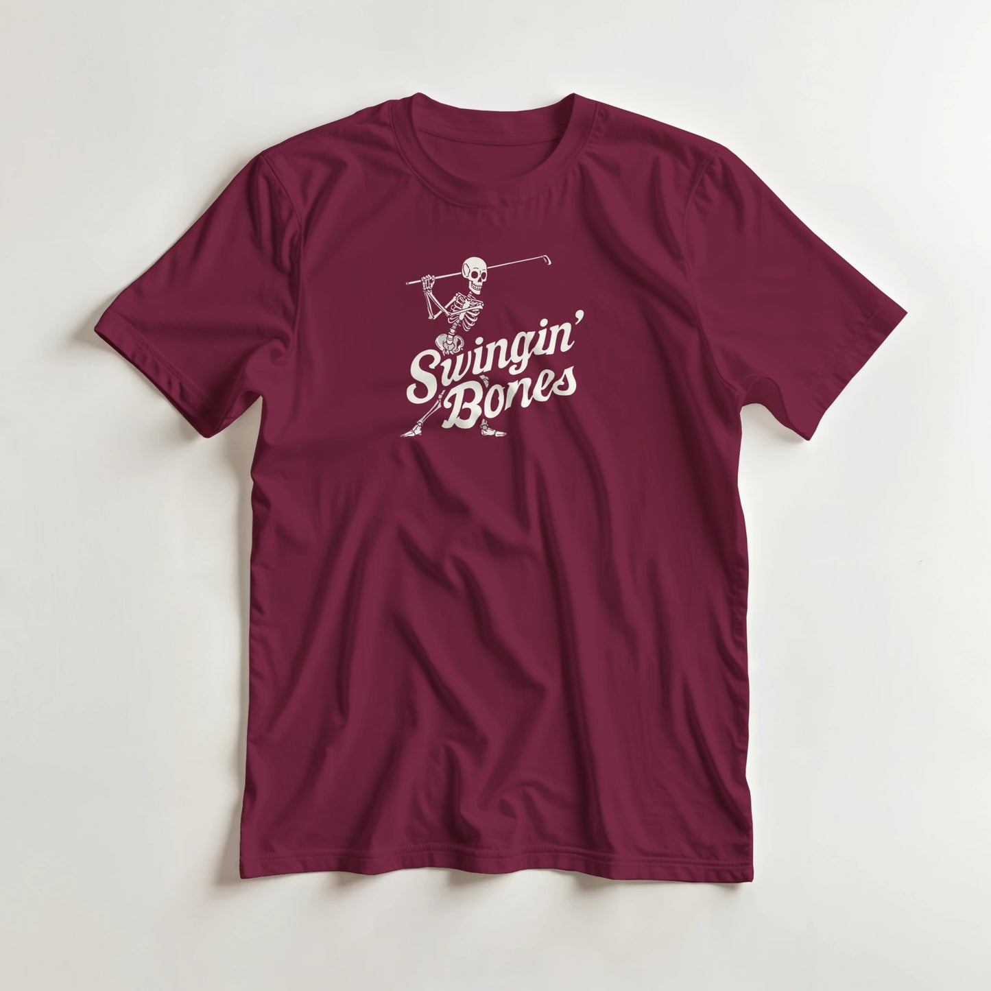 Swingin' Bones T-Shirt in Maroon M lying on a plain floor. T-shirt is a unisex cut and 100 per cent cotton.