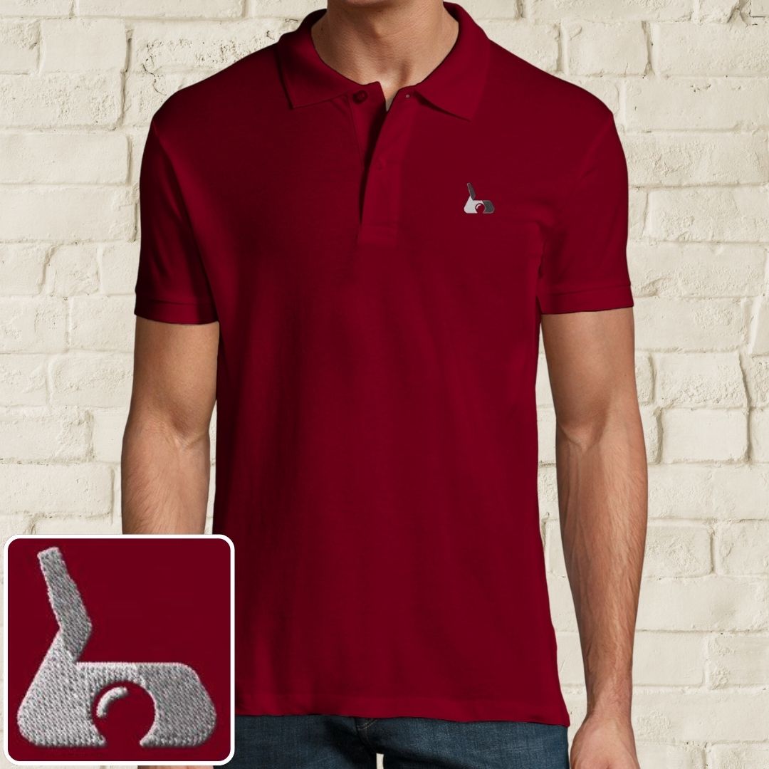 Putter Polo in Maroon on a light wooden floor lying next to headphones and golf shoes.