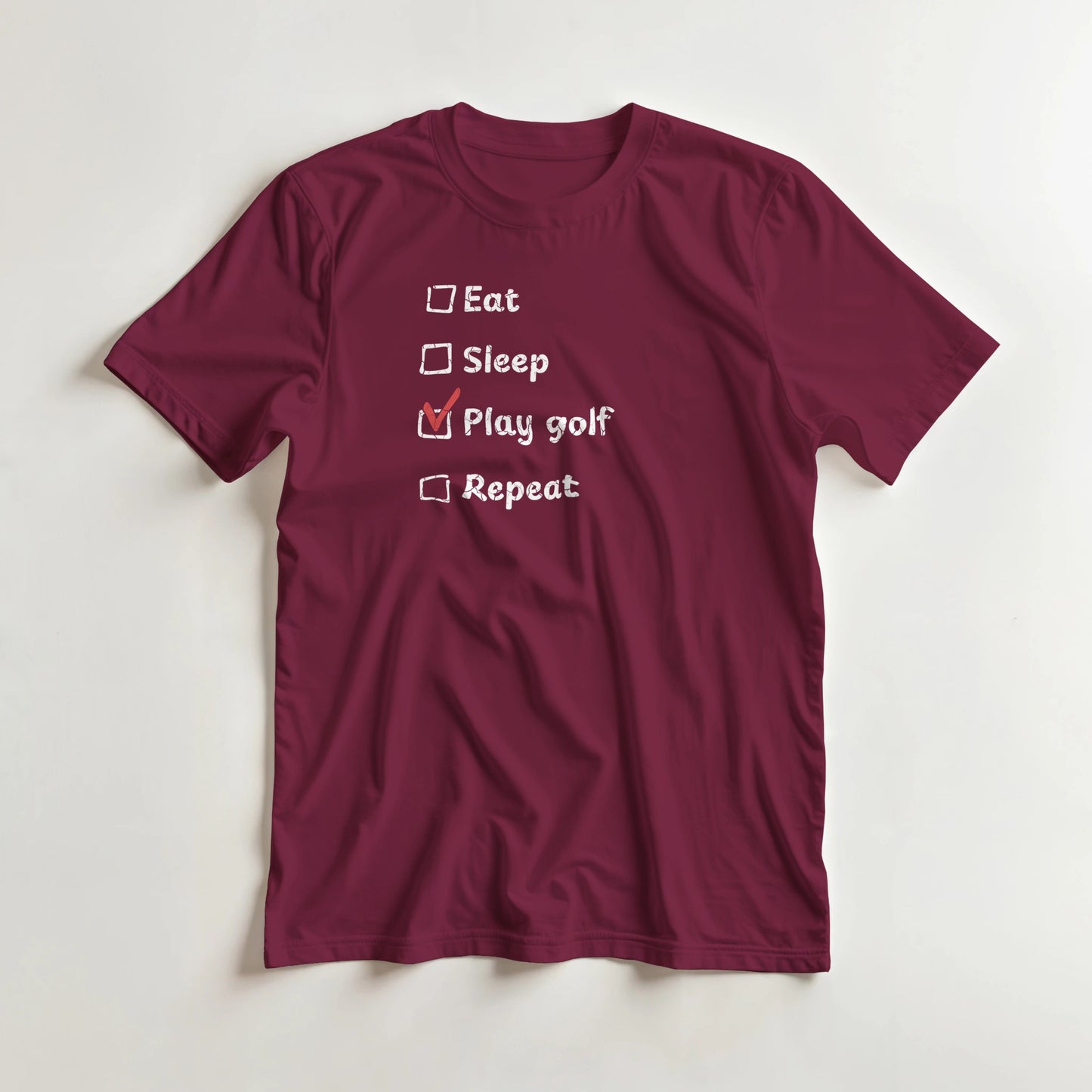 Golf Repeat T-Shirt in Maroon lying on a plain floor. T-shirt is a unisex cut and 100 per cent cotton.