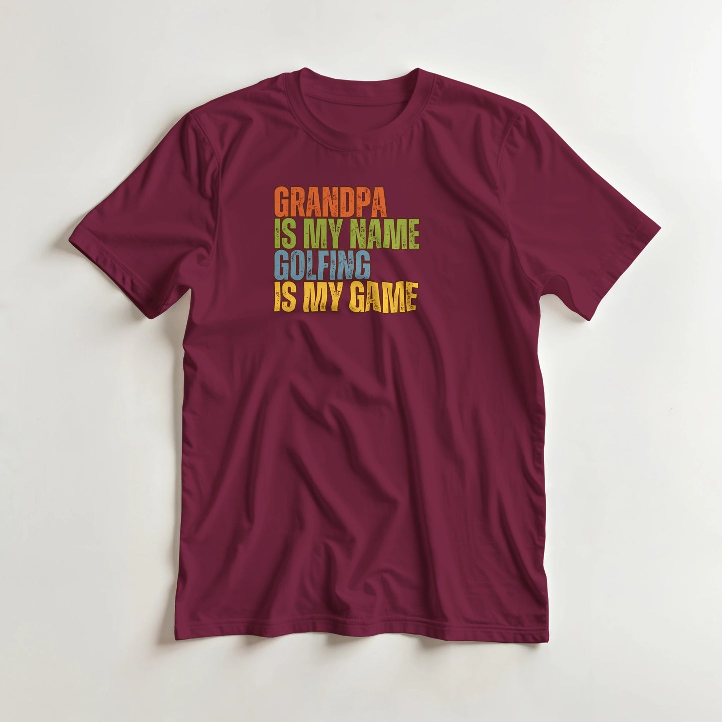 Grandpa Golfing T-Shirt in Maroon lying on a plain floor. T-shirt is a unisex cut and 100 per cent cotton.