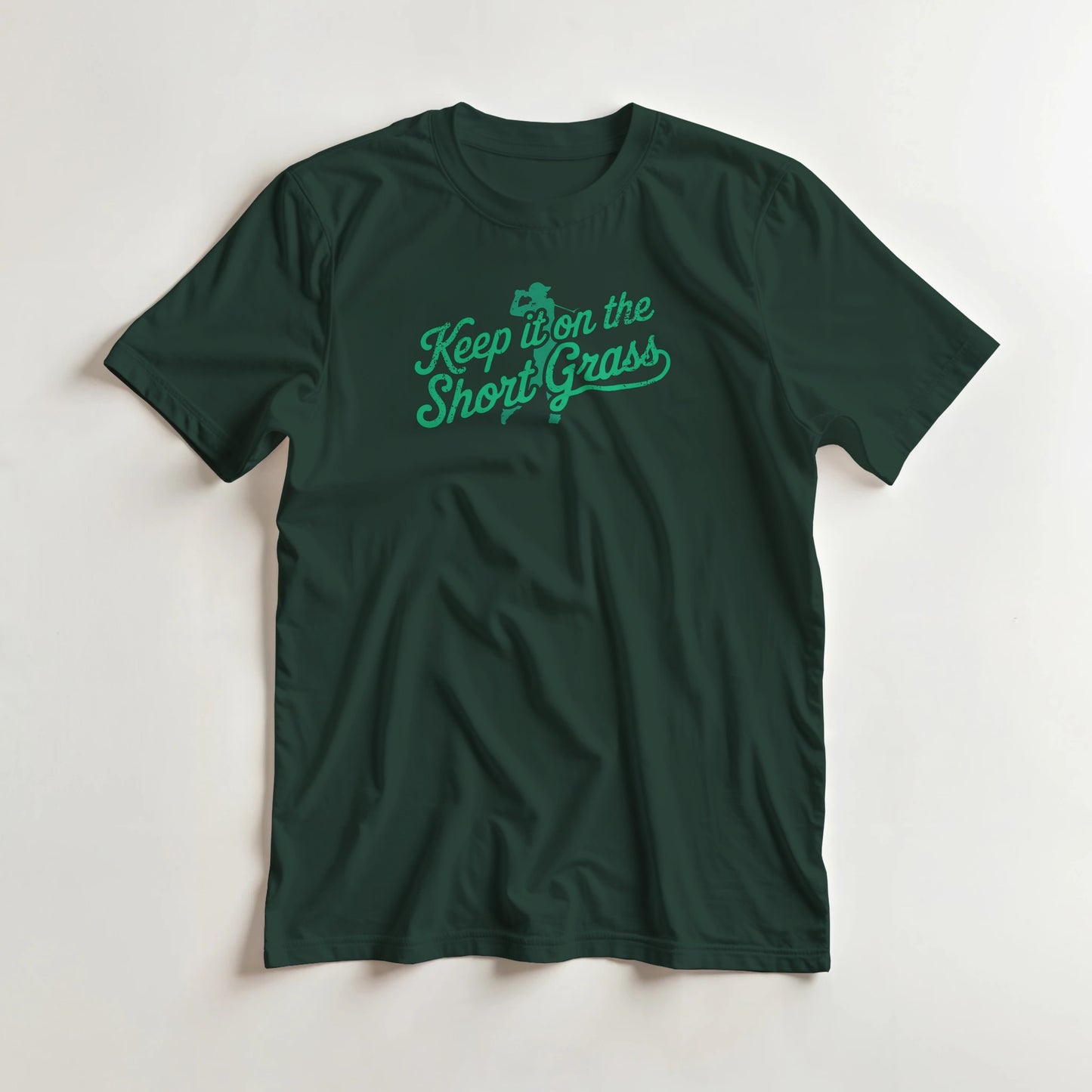 Short Grass T-Shirt in Forest Green lying on a plain floor. T-shirt is a unisex cut and 100 per cent cotton.