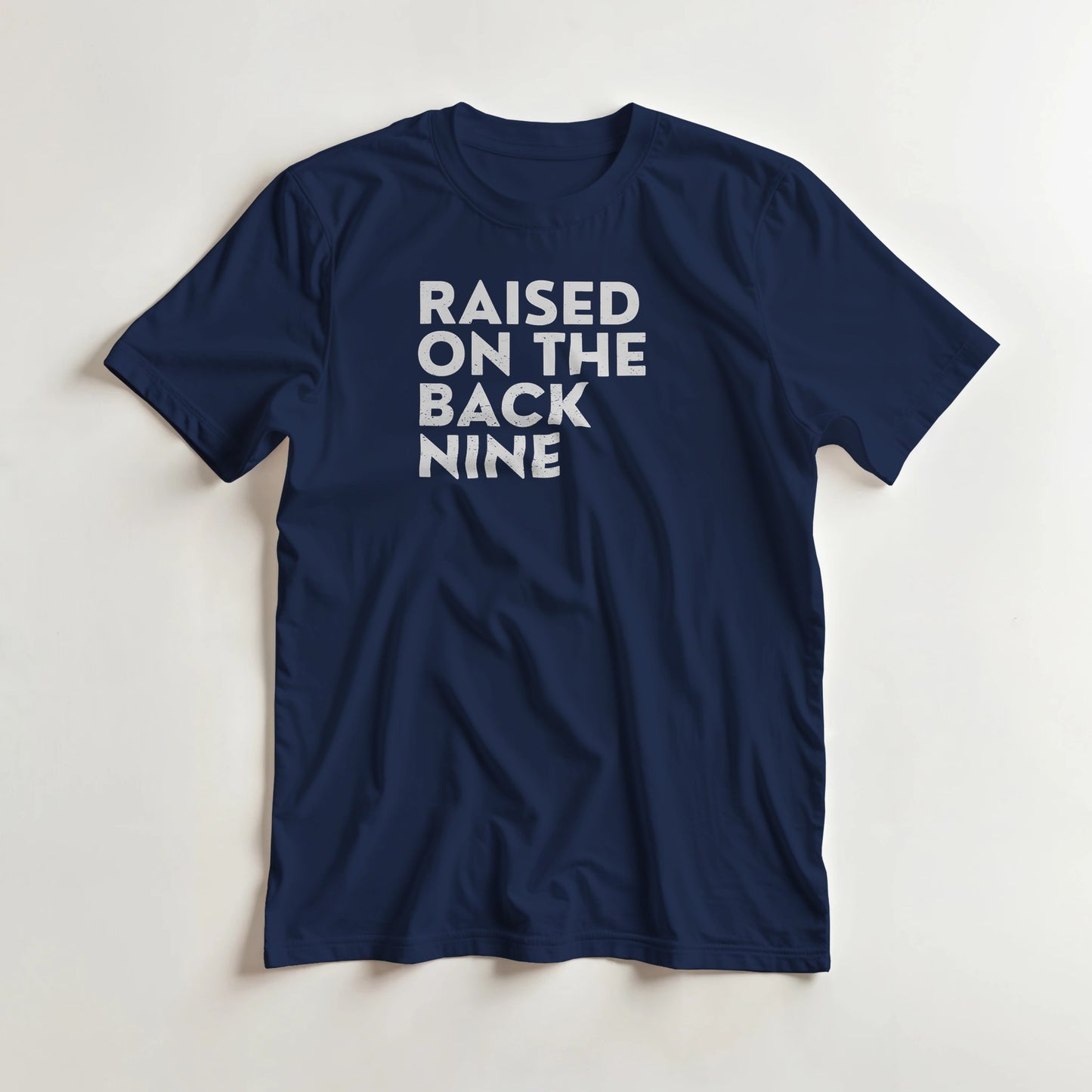 Raised On T-Shirt in Navy lying on a plain floor. T-shirt is a unisex cut and 100 per cent cotton.
