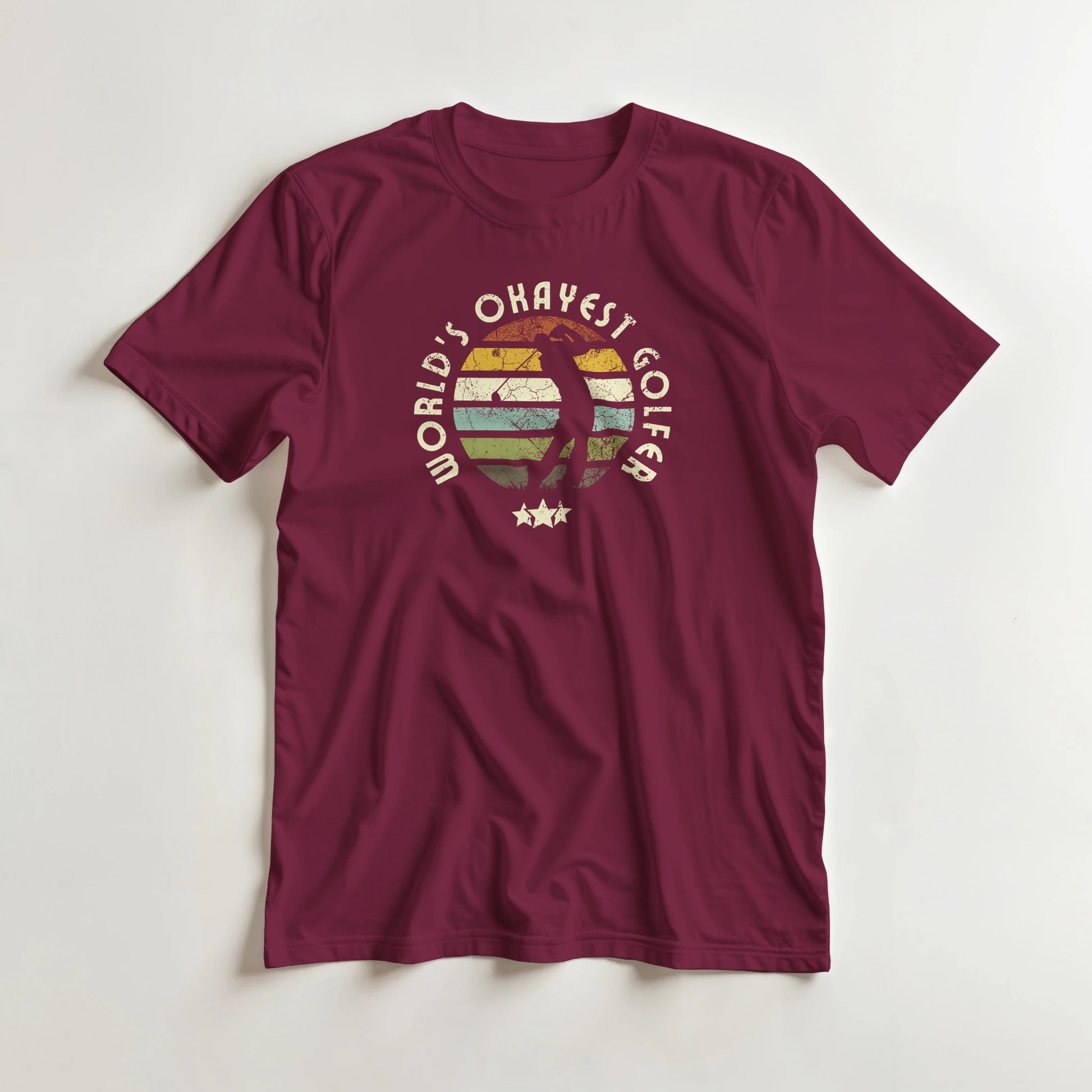Okayest Golfer T-Shirt in Maroon lying on a plain floor. T-shirt is a unisex cut and 100 per cent cotton.