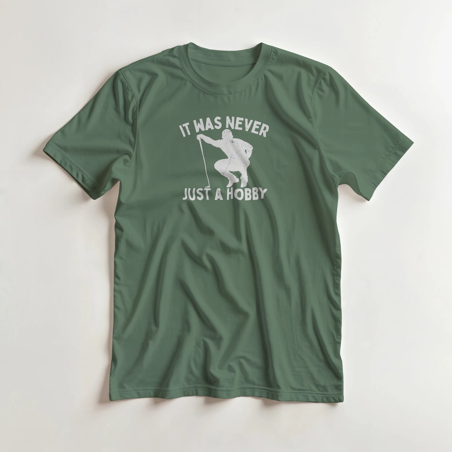 Just A Hobby T-Shirt in Military Green lying on a plain floor. T-shirt is a unisex cut and 100 per cent cotton.