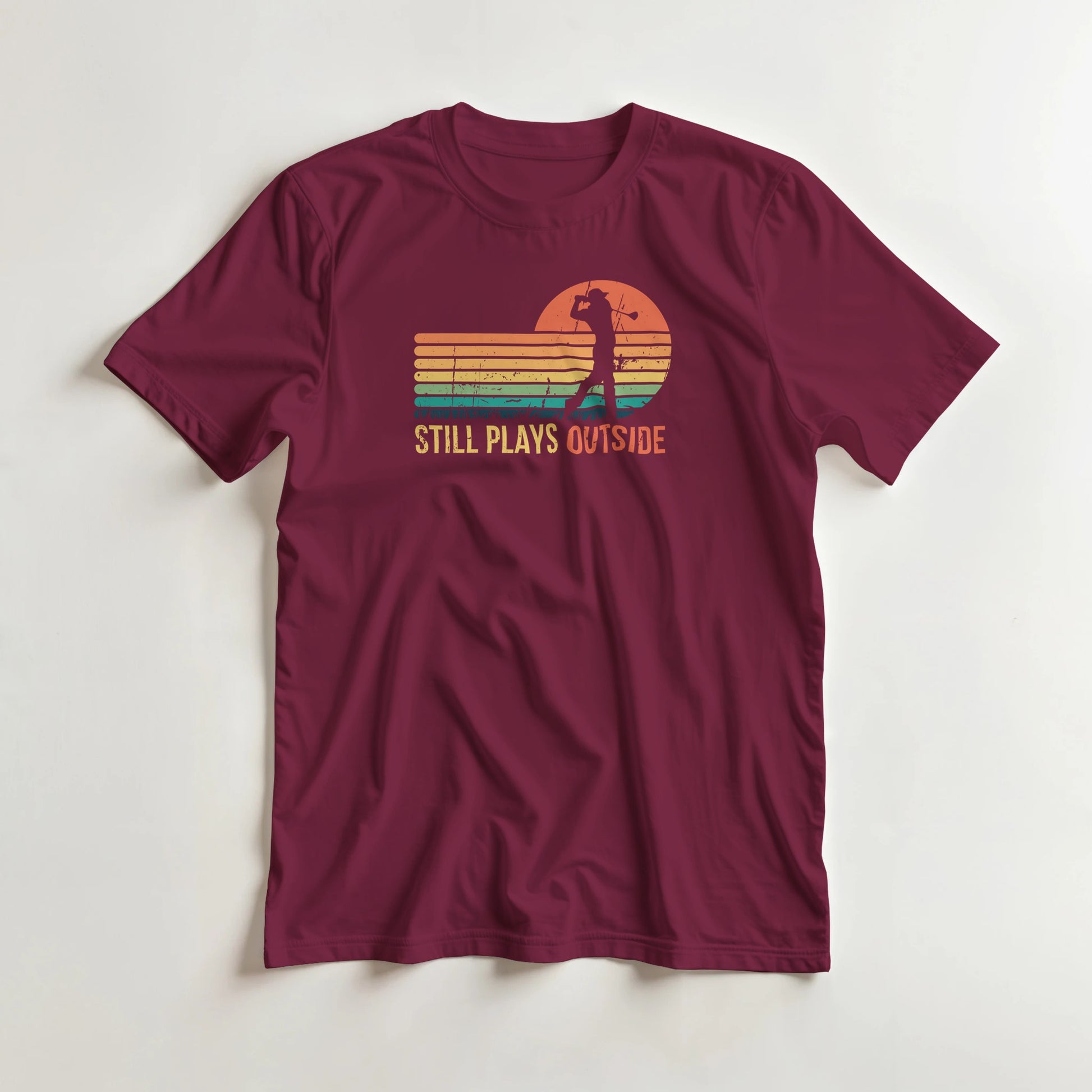 Plays Outside T-Shirt in Maroon S lying on a plain floor. T-shirt is a unisex cut and 100 per cent cotton.
