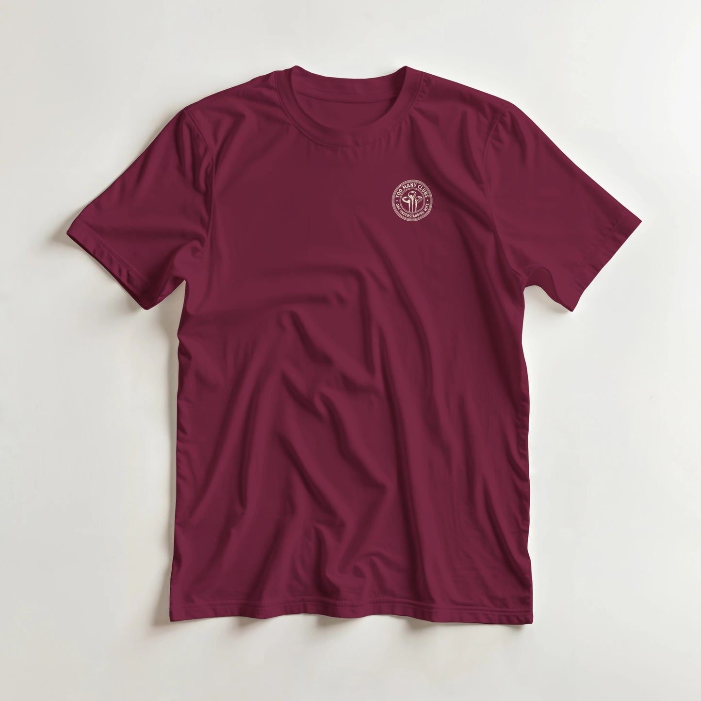 Too Many Clubs Pocket T-Shirt in Maroon lying on a plain floor. T-shirt is a unisex cut and 100 per cent cotton.