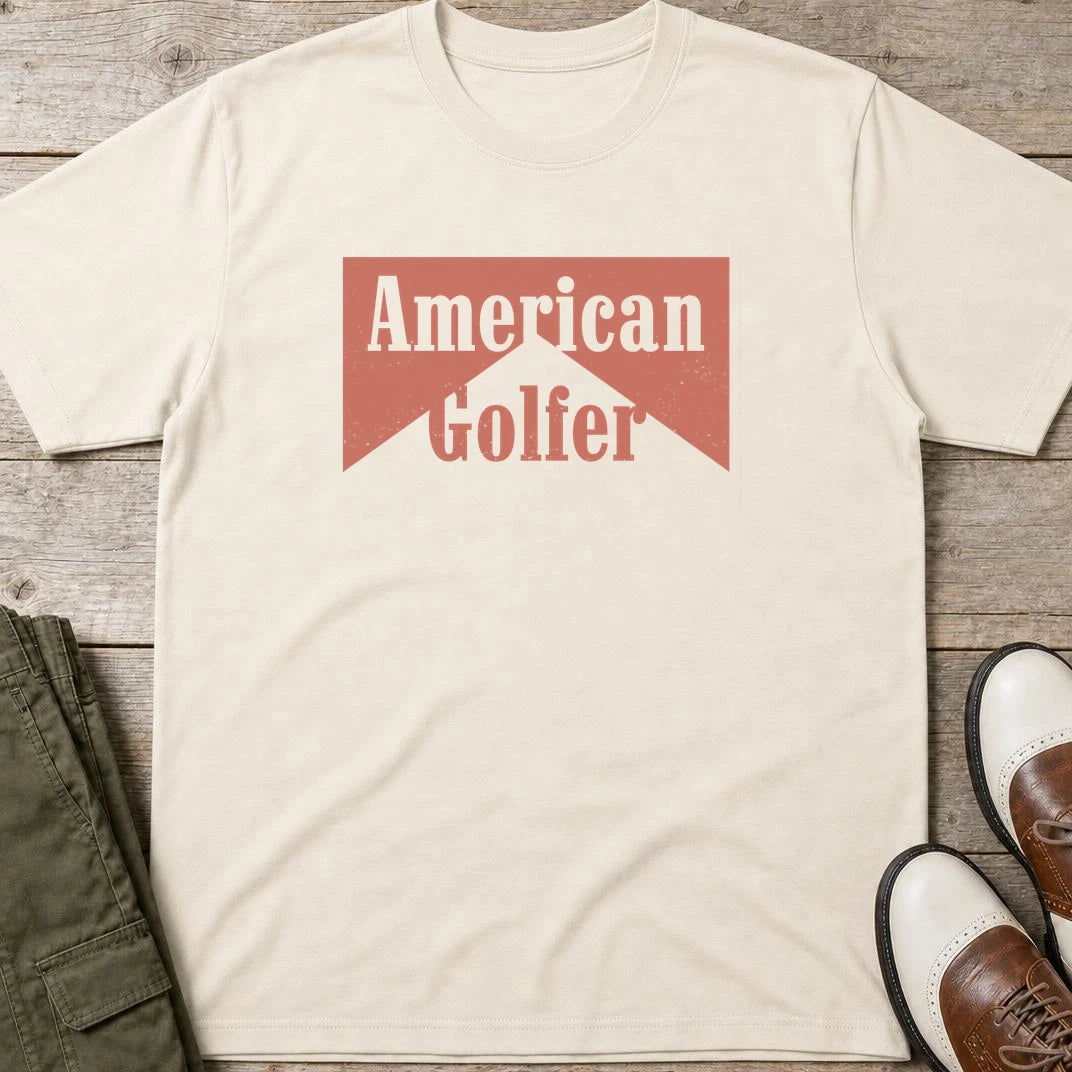 American Golfer T-Shirt in Natural lying on a plain floor. T-shirt is a unisex cut and 100 per cent cotton.