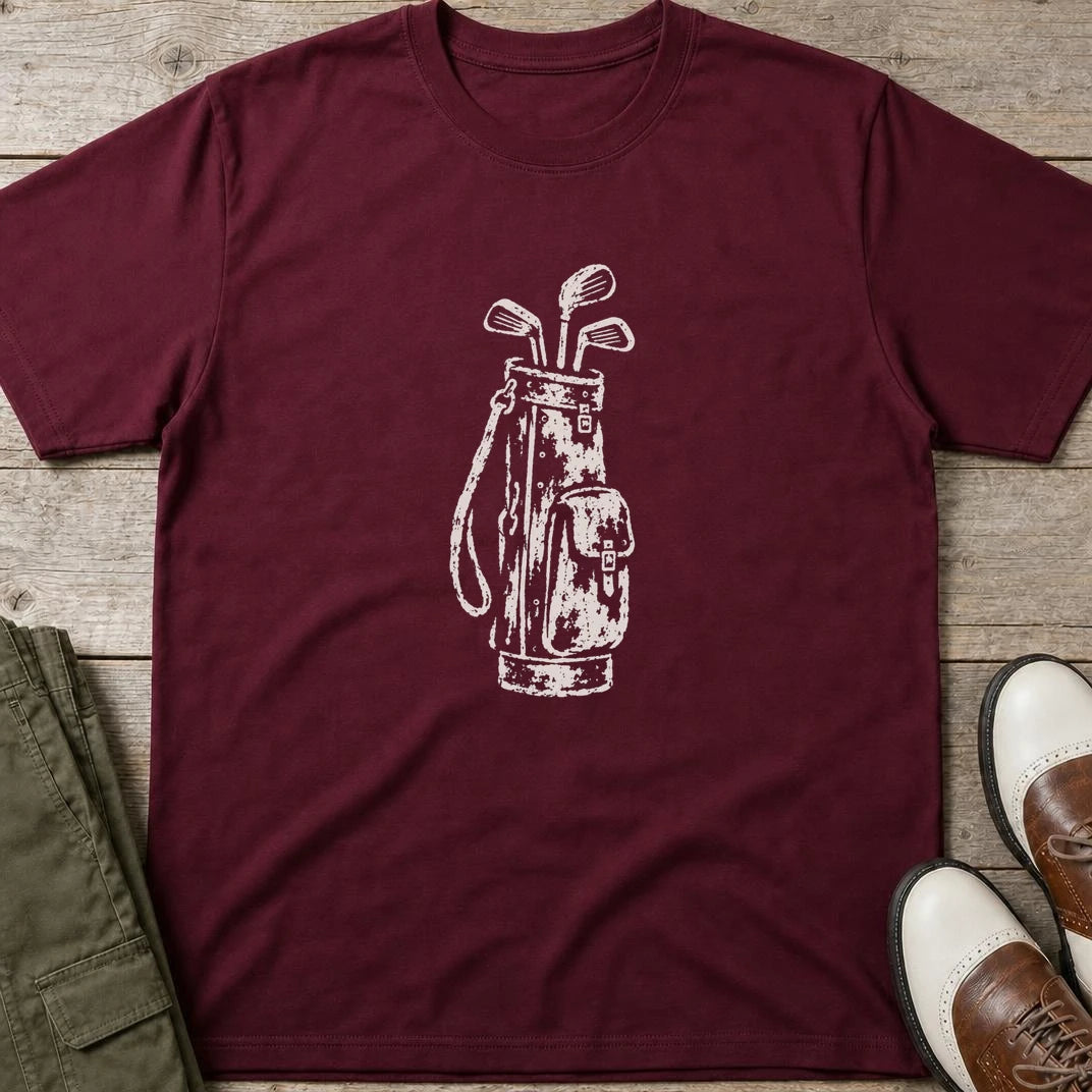 Vintage Golf Bag T-Shirt in Maroon lying on a plain floor. T-shirt is a unisex cut and 100 per cent cotton.