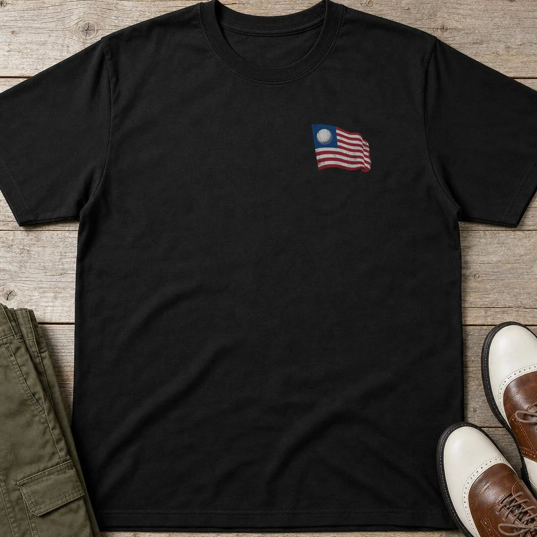 Golf Flag Pocket T-Shirt in Black lying on a plain floor. T-shirt is a unisex cut and 100 per cent cotton.