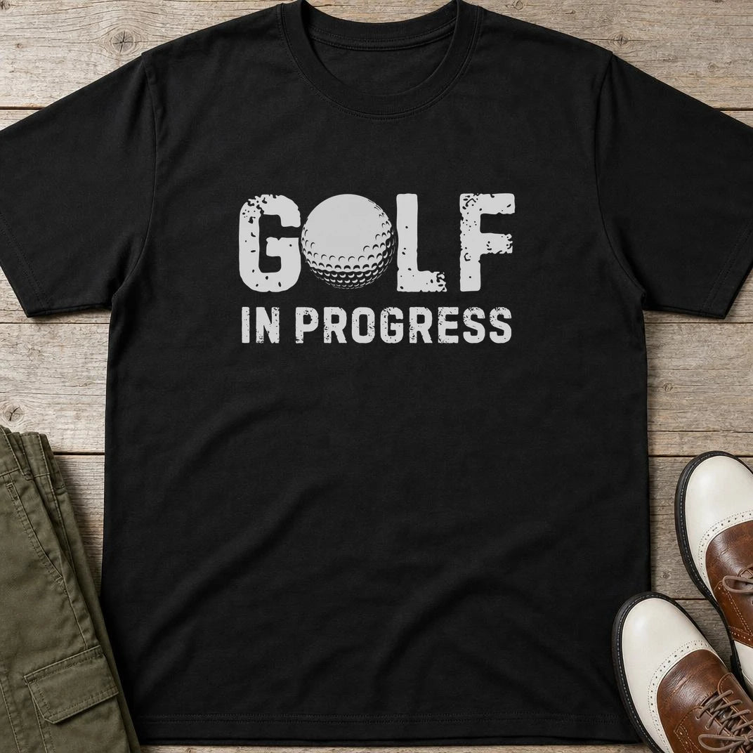 Golf In Progress T-Shirt in Black lying on a plain floor. T-shirt is a unisex cut and 100 per cent cotton.