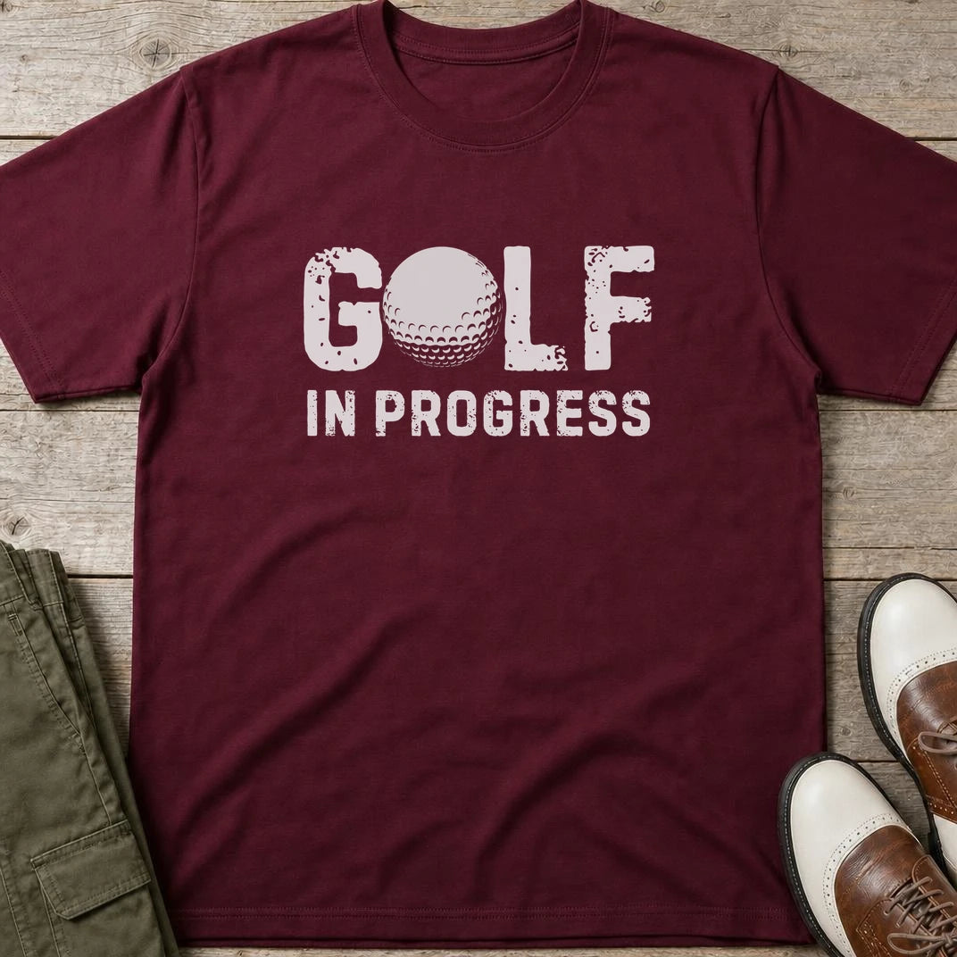 Golf In Progress T-Shirt in Maroon lying on a plain floor. T-shirt is a unisex cut and 100 per cent cotton.