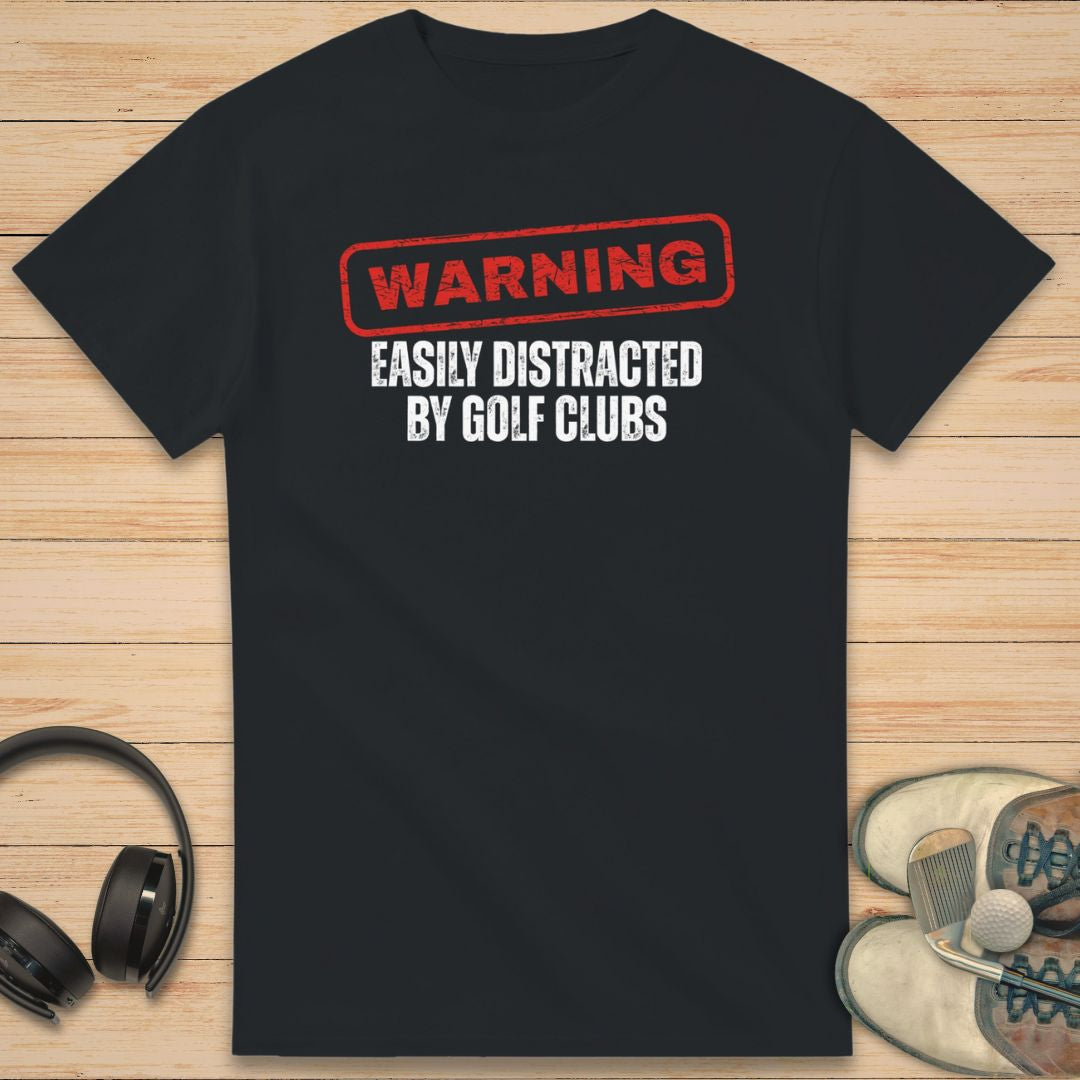 Warning T-Shirt in Black on a light wooden floor lying next to headphones and golf shoes.