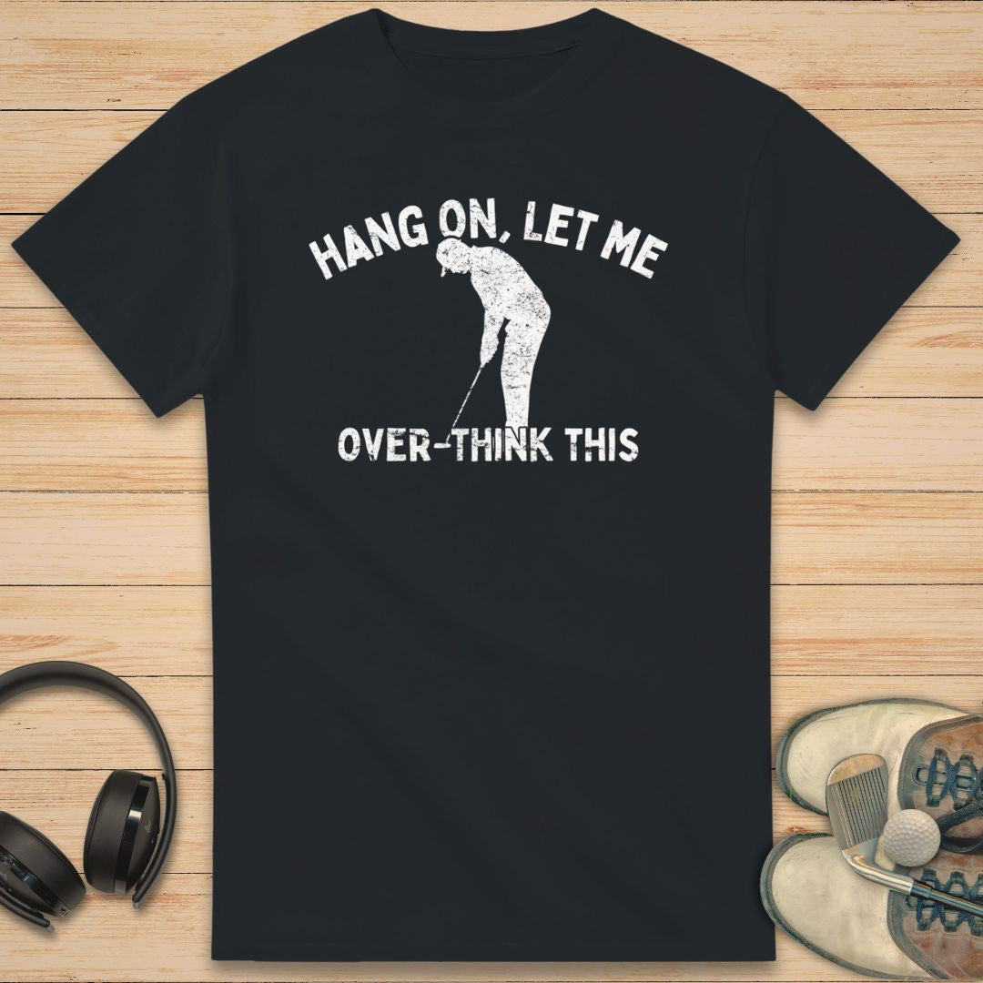 Over-Think T-Shirt in Black on a light wooden floor lying next to headphones and golf shoes.