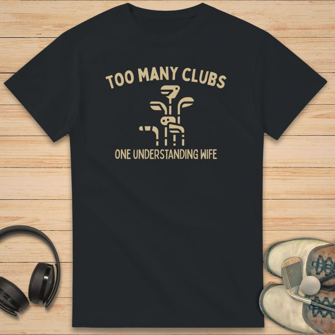 Understanding Wife T-Shirt in Black on a light wooden floor lying next to headphones and golf shoes.