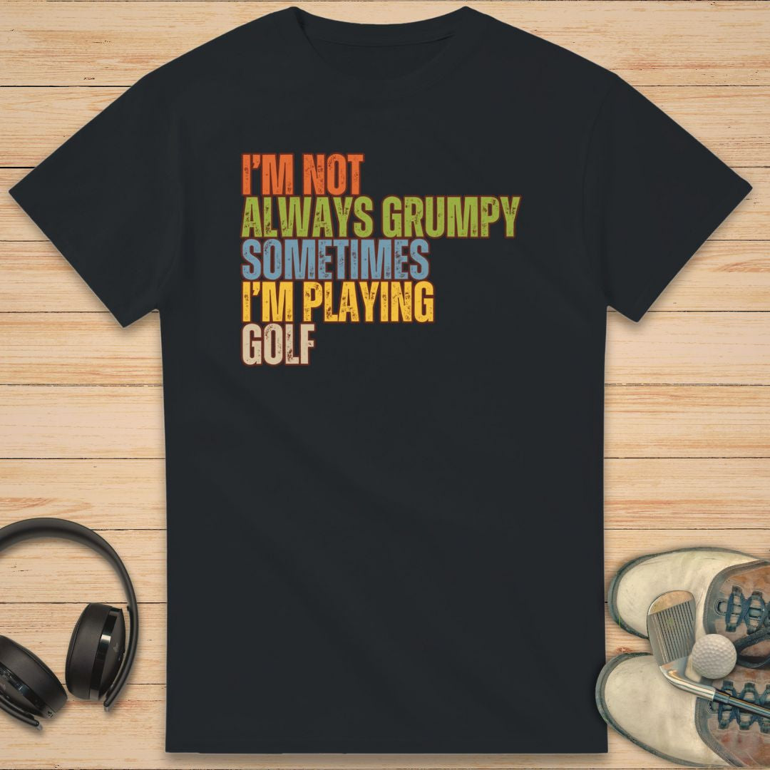 Grumpy Classic T-Shirt in Black on a light wooden floor lying next to headphones and golf shoes.