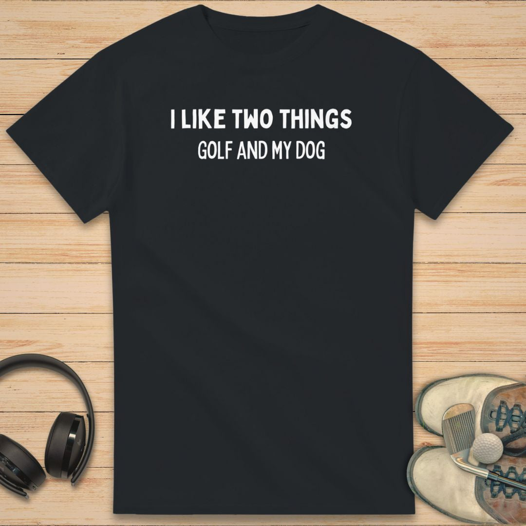 Two Things T-Shirt in Black on a light wooden floor lying next to headphones and golf shoes.