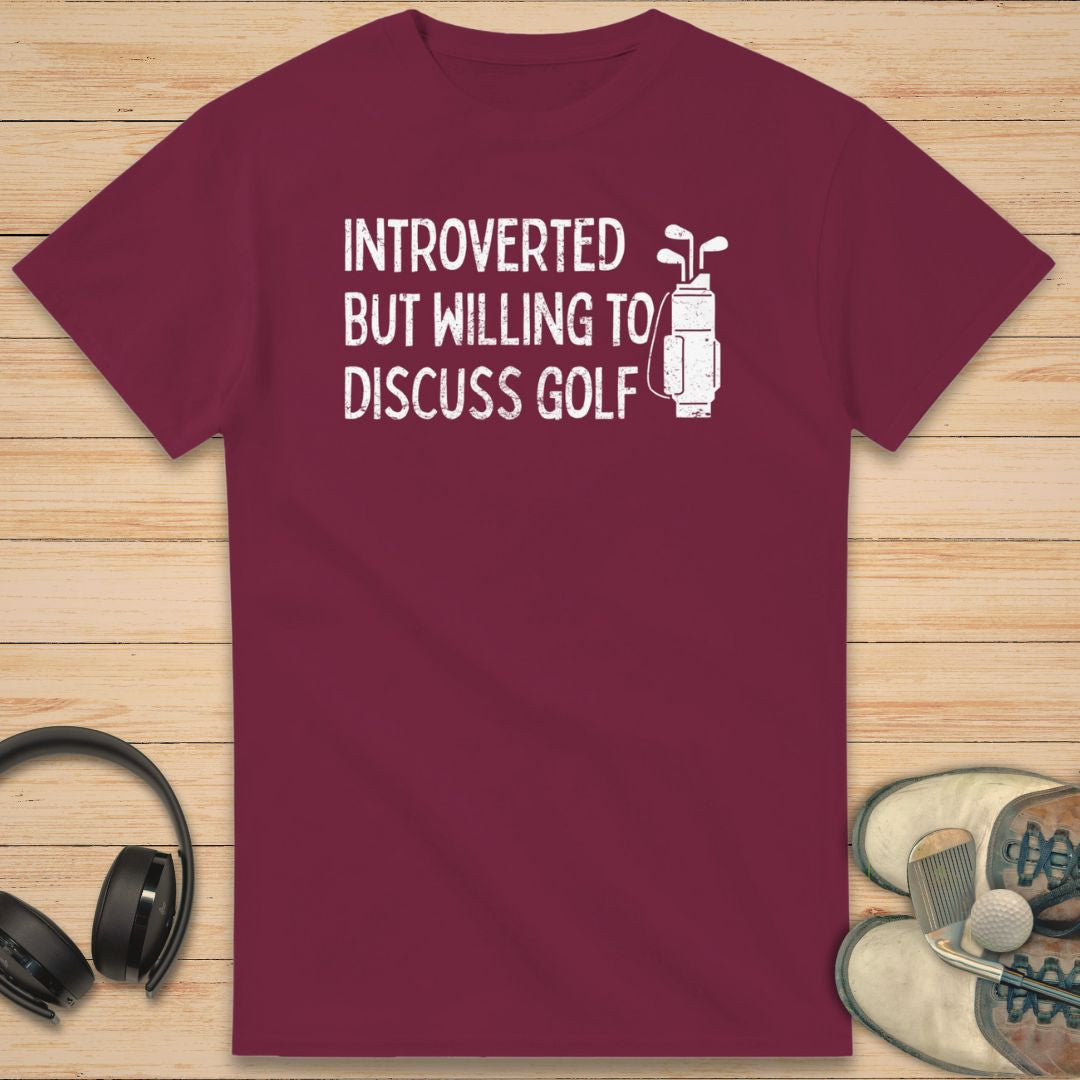 Introverted T-Shirt in Maroon on a light wooden floor lying next to headphones and golf shoes.