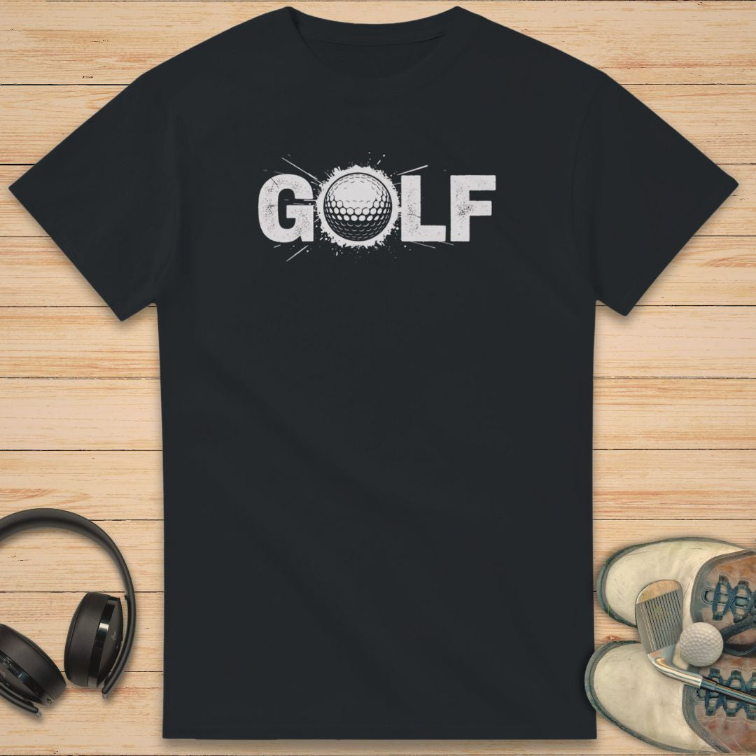 Golf Crash T-Shirt in Black on a light wooden floor lying next to headphones and golf shoes.