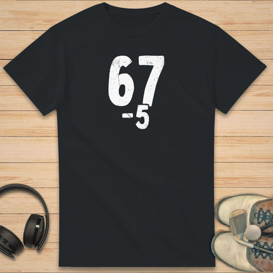67 5 Under T-Shirt in Black on a light wooden floor lying next to headphones and golf shoes.