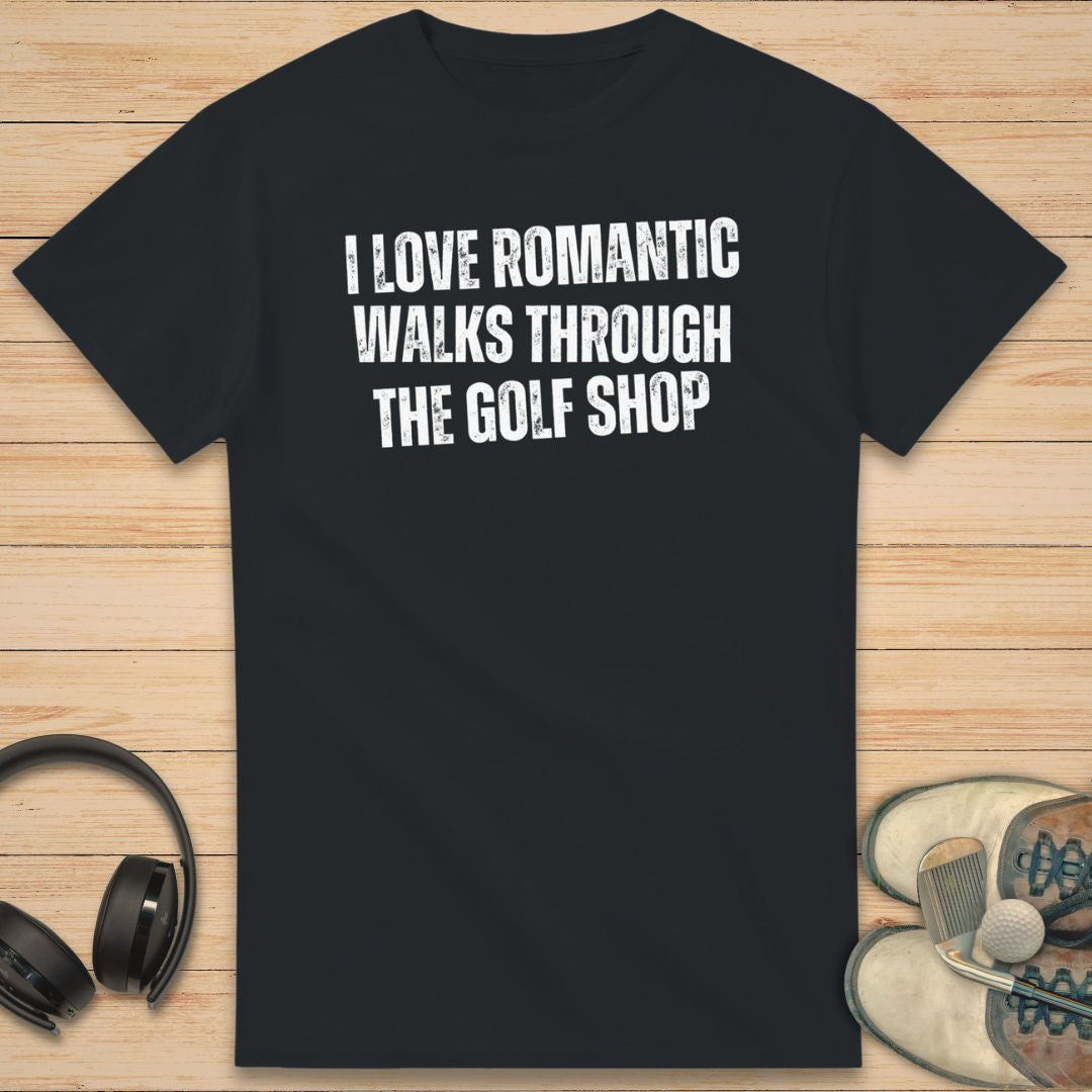 Romantic Walks T-Shirt in Black on a light wooden floor lying next to headphones and golf shoes.