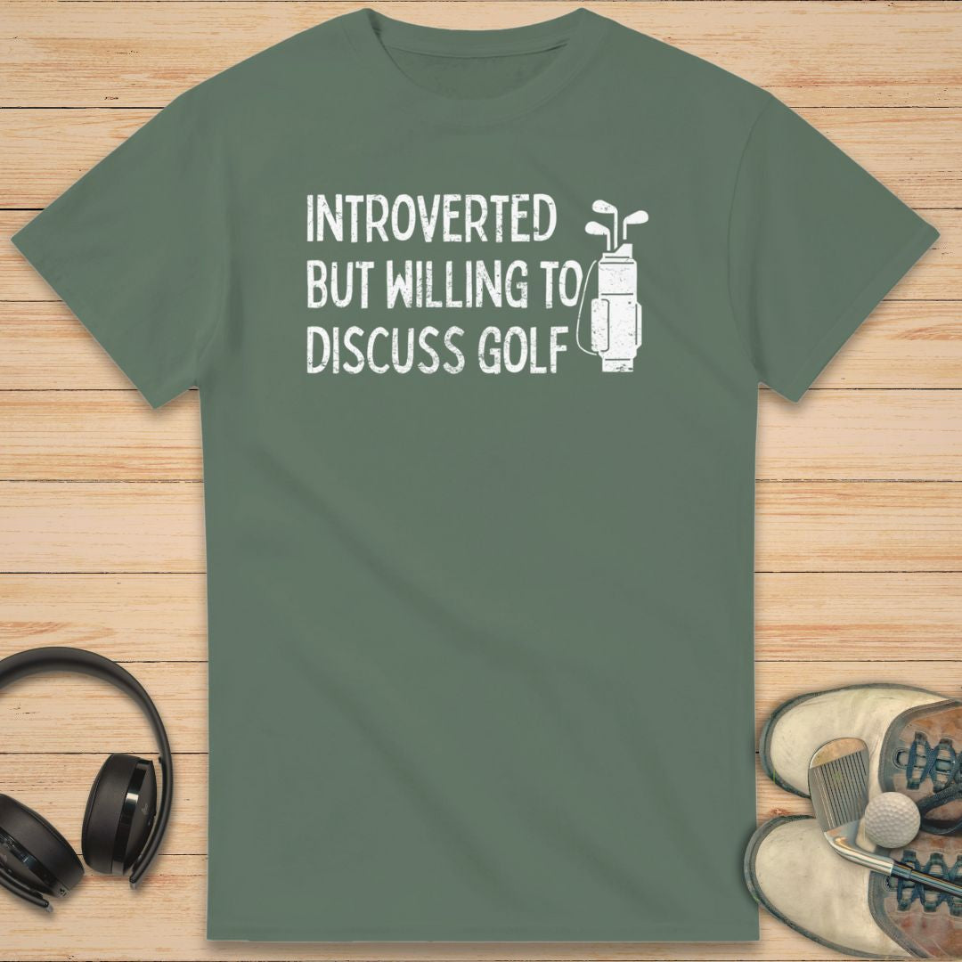 Introverted T-Shirt in Military Green on a light wooden floor lying next to headphones and golf shoes.