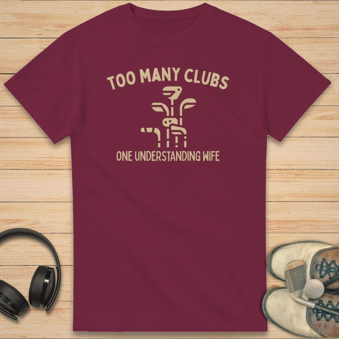 Understanding Wife T-Shirt in Maroon on a light wooden floor lying next to headphones and golf shoes.